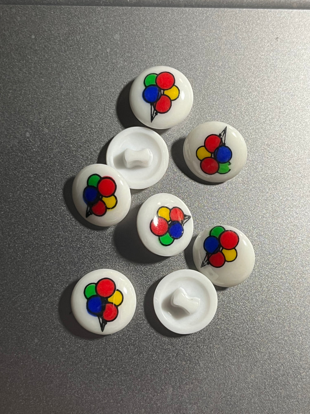 White buttons with colorful balloon designs on a gray surface