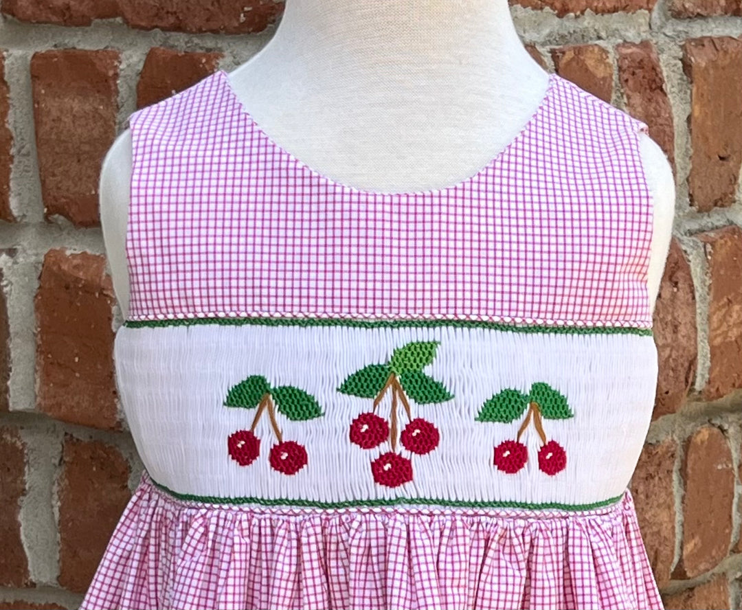 Mannequin wearing a pink checkered dress with cherry design against a brick wall.