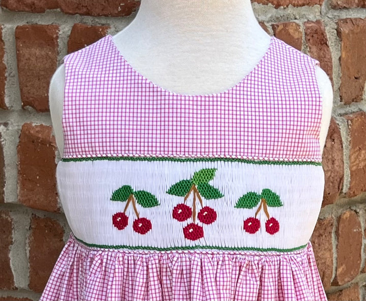 Mannequin wearing a pink checkered dress with cherry design against a brick wall.