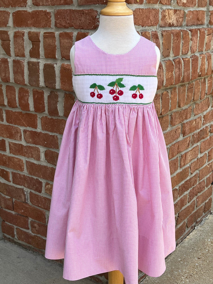 Pink checkered dress with cherry design on a mannequin against a brick wall.