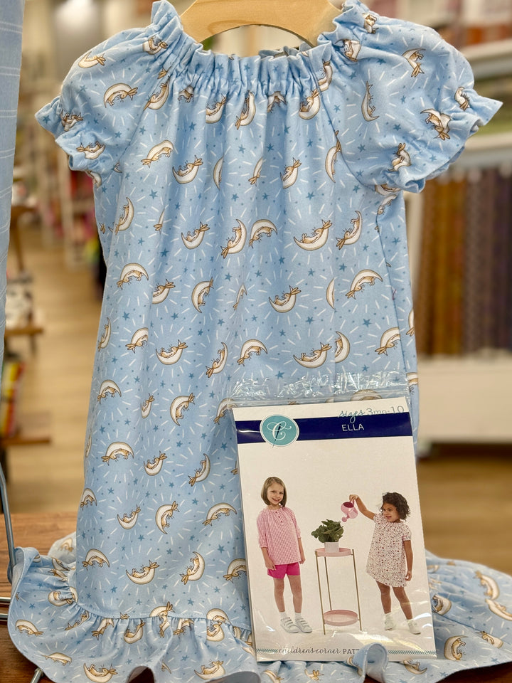 blue flannel nightgown.  fabric is covered with bunnies, white half moons and blue stars.  A wooden hanger is present along with the Children's Corner pattern Ella.