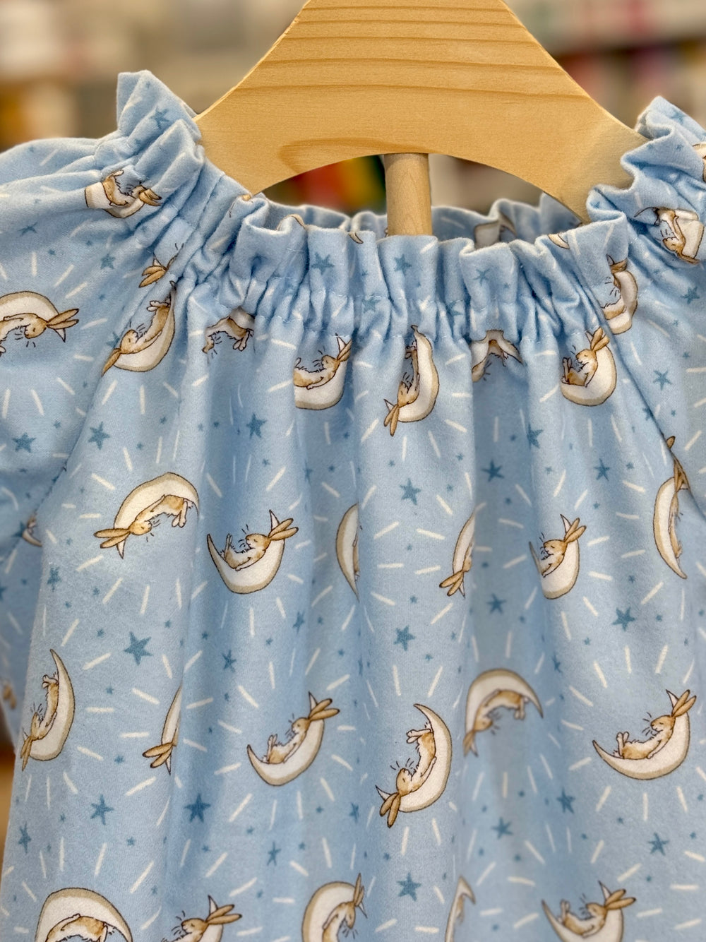 blue flannel nightgown with elastic at the neck on a wooden hanger.  fabric is covered in tan bunnies laying in white half moons