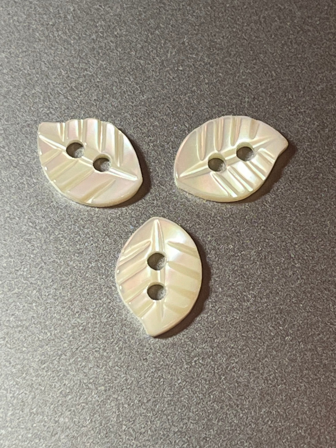 Three leaf-shaped buttons with a textured pattern on a gray surface
