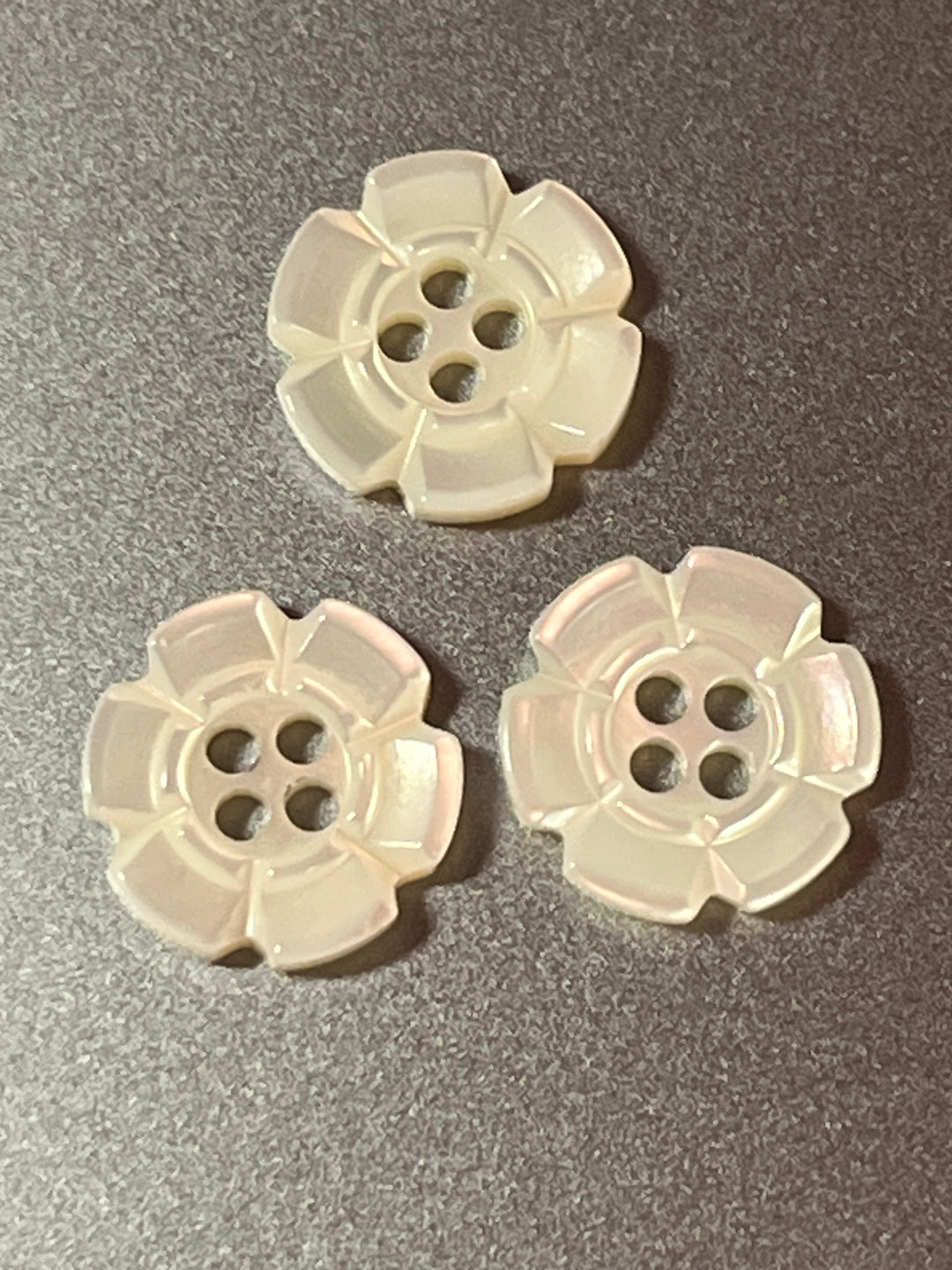 Three white floral buttons on a gray background