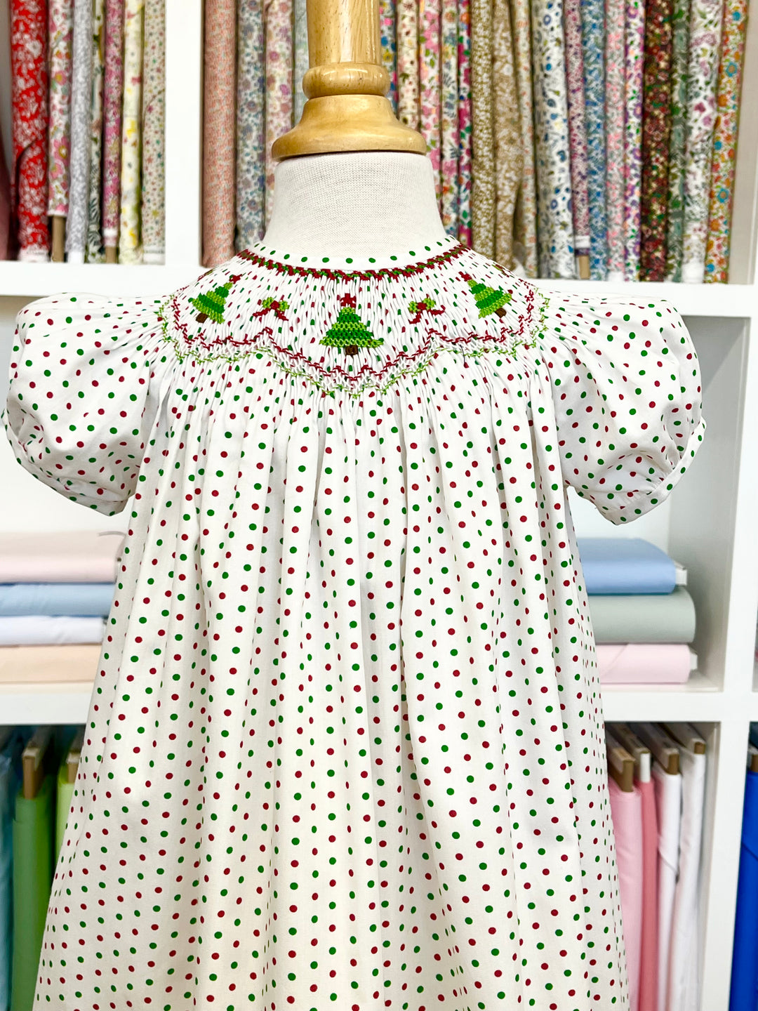 Christmas trees smocked on a bishop dress on a mannequin against a fabric background