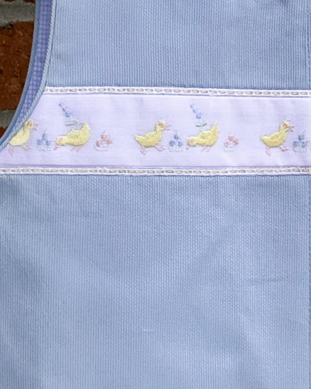 Light blue fabric with embroidered yellow duck designs on a textured surface