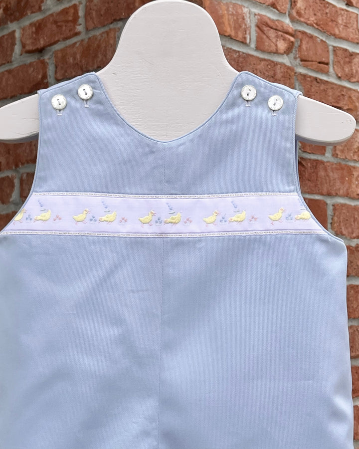 Light blue children's dress with white buttons on a mannequin against a brick wall.