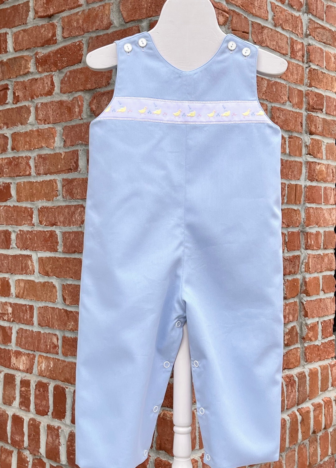 Light blue children's overalls on a mannequin against a brick wall.