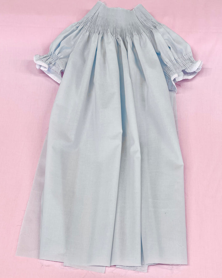 Light blue dress with smocked sleeves on a pink background