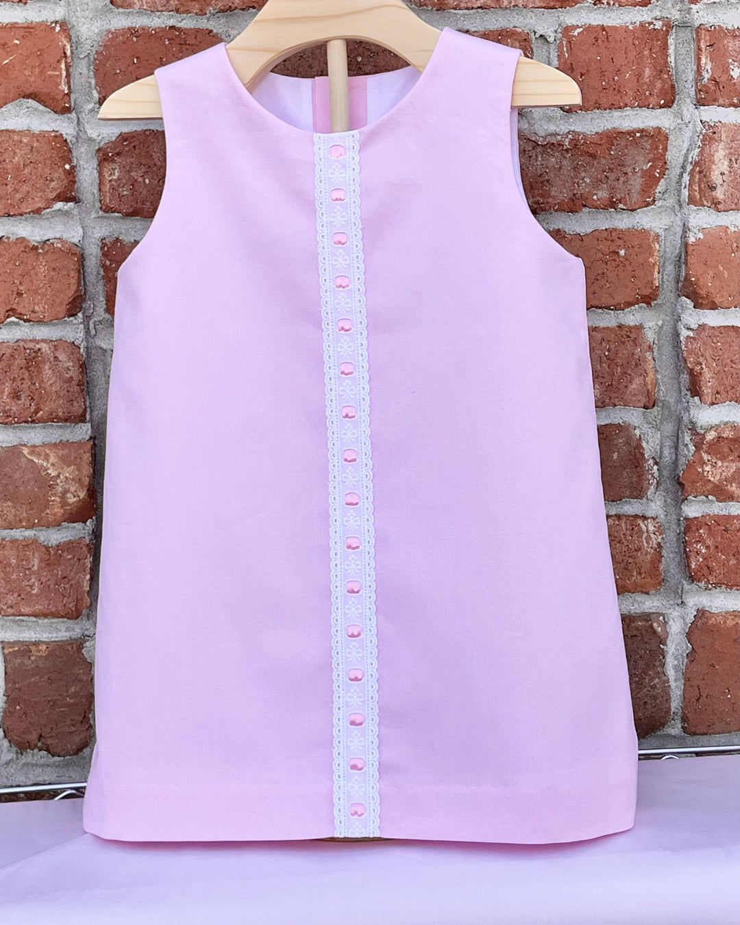 Light purple sleeveless top with button details on a hanger against a brick wall.