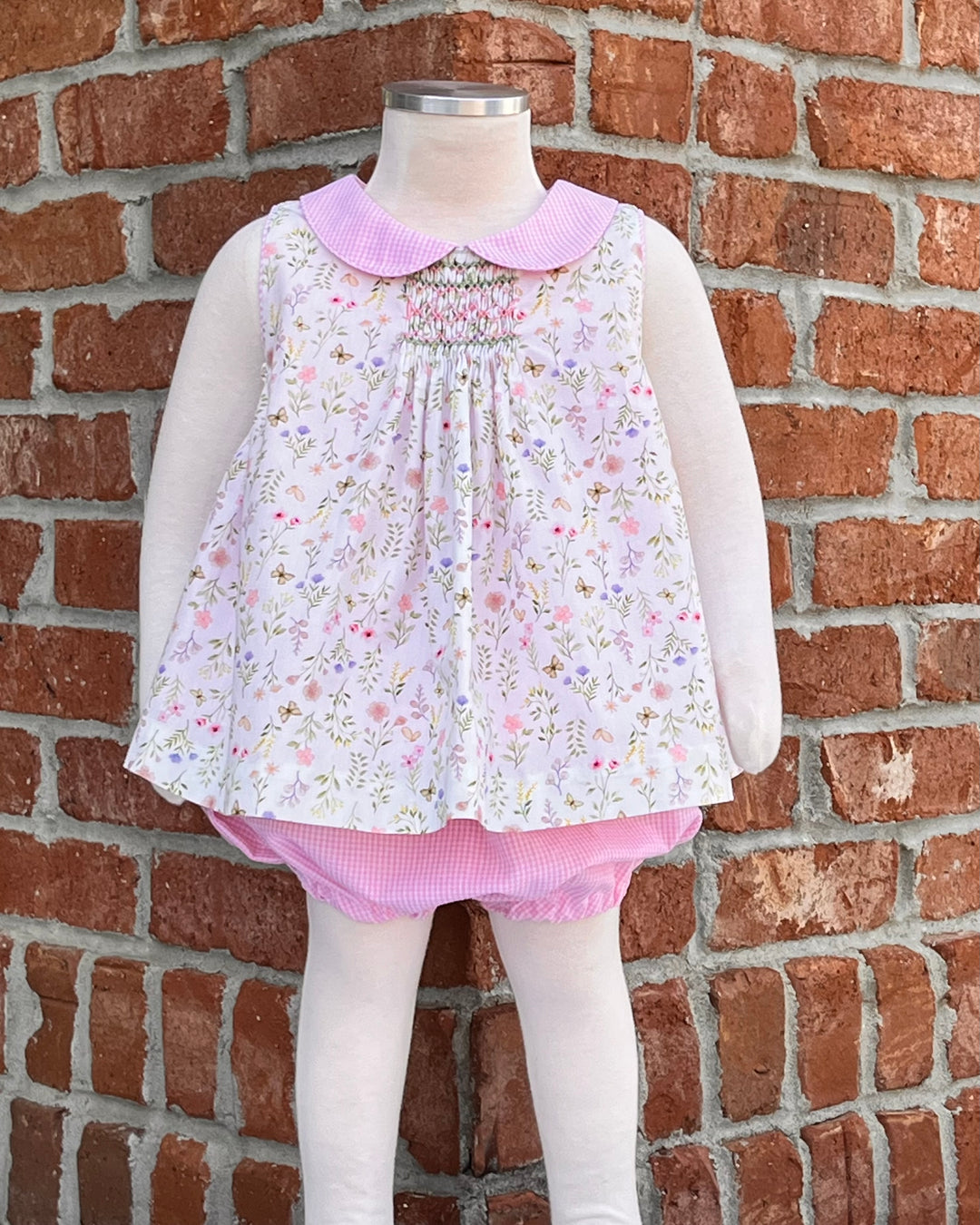 smocked top with pink gingham collar and bloomers against a brick background