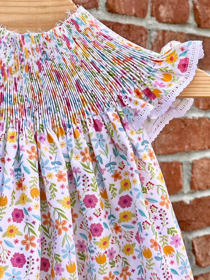 Colorful floral-patterned dress with lace trim hanging against a brick wall.