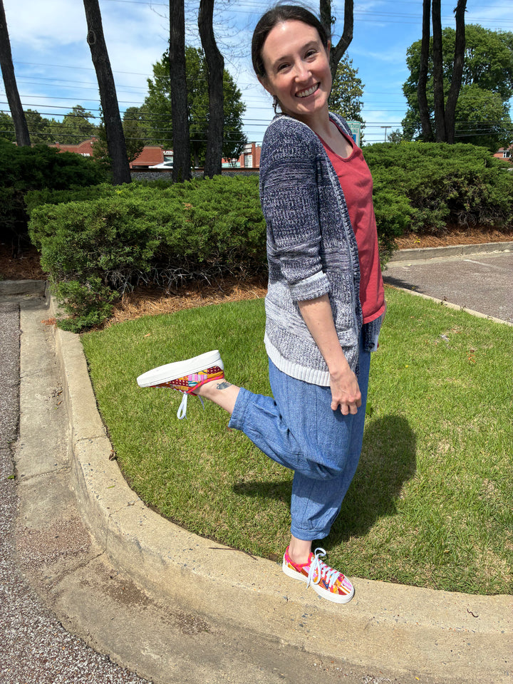 Woman standing on grass with a shoe in her hand, smiling outdoors.
