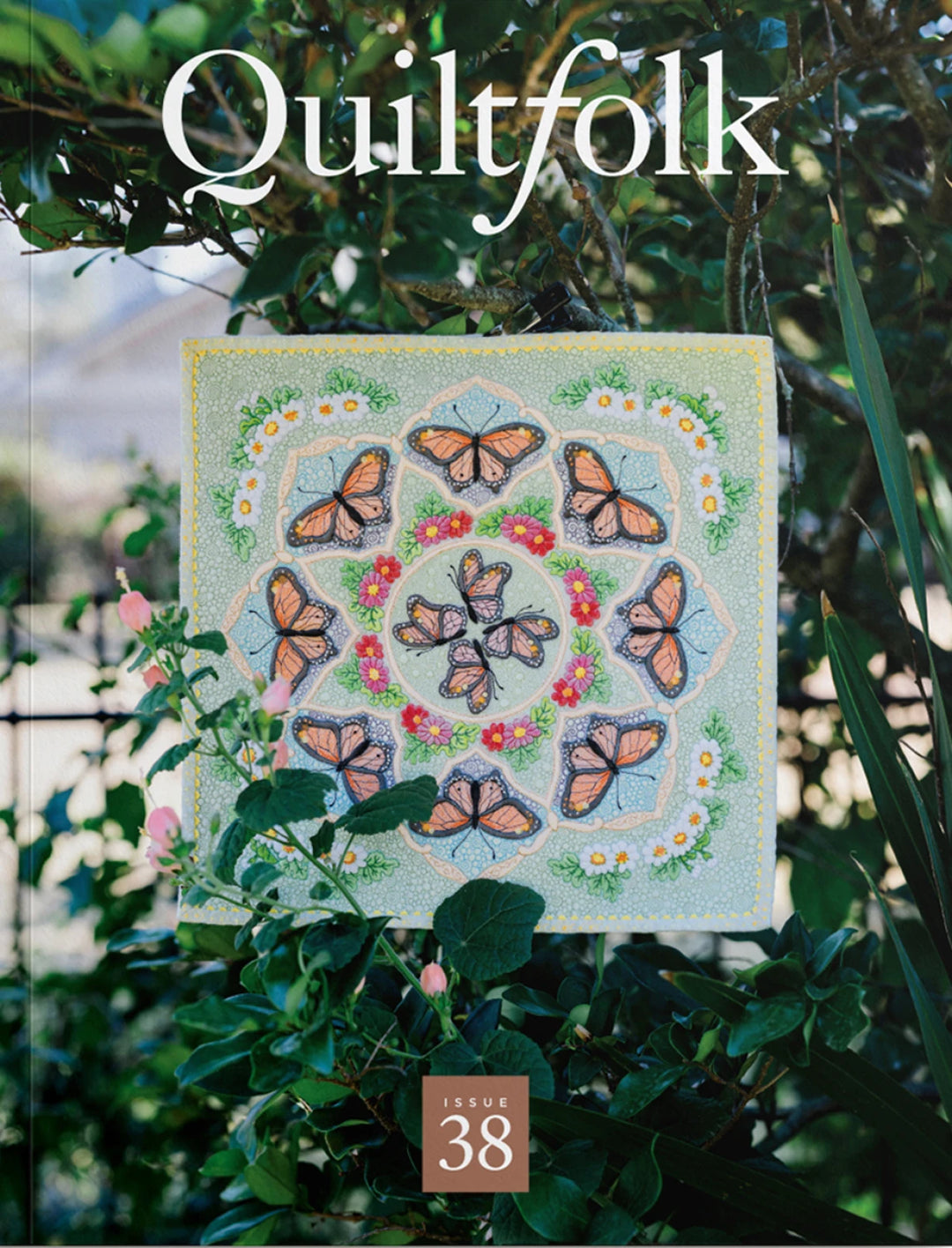 Quilt with butterfly design on a magazine cover titled 'Quiltfolk' Issue 38, surrounded by greenery.