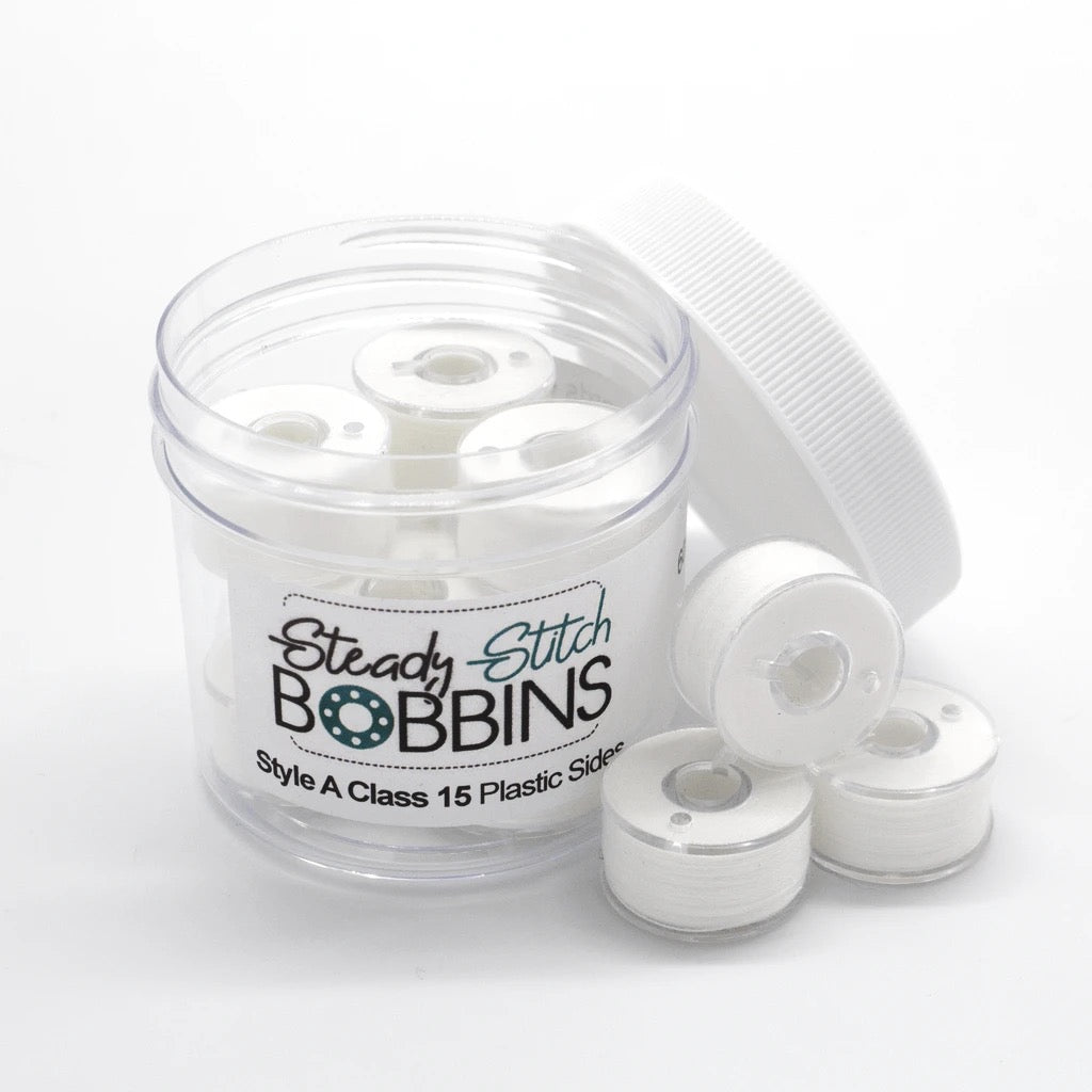 A clear plastic jar labeled 'Steady Stitch BOBBINS' containing white plastic bobbin spools, with several white bobbins placed outside the jar on a clean white background.
