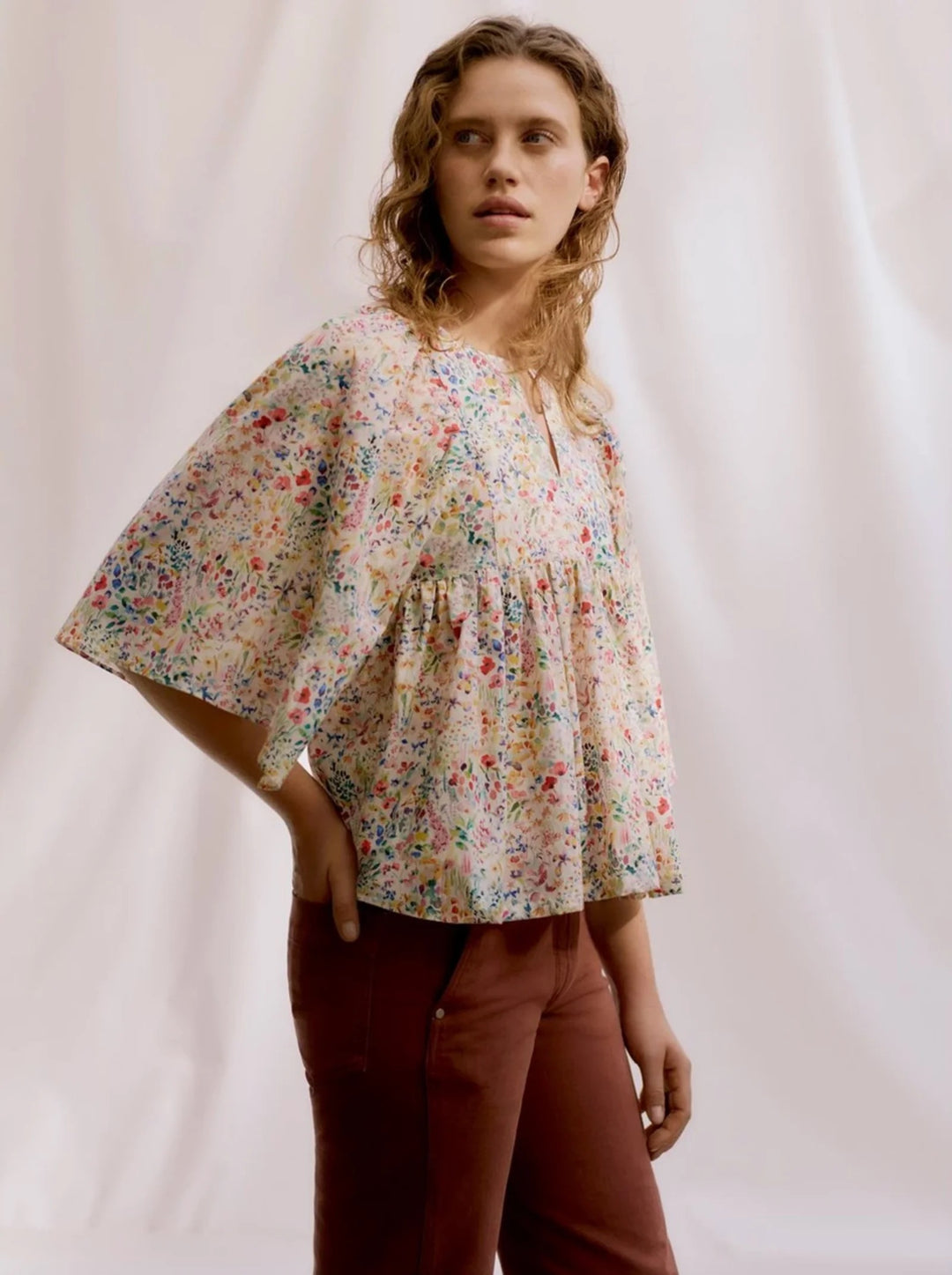 Woman wearing a floral blouse and brown pants against a plain background