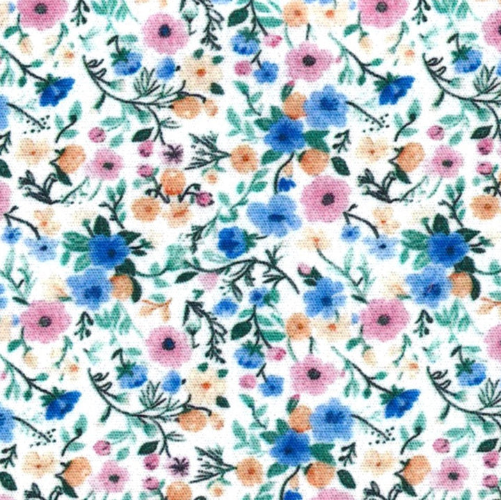 A close-up of a white fabric with a dense, repeating floral pattern featuring blue, pink, orange, and green flowers and leaves.
