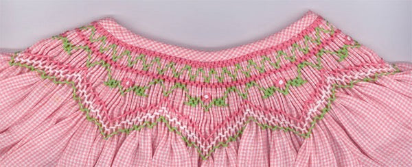 Close-up of a pink dress with smocked neckline and green embroidery on a gray background