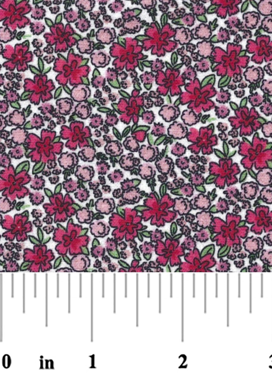 A close-up of a floral fabric pattern featuring pink and magenta flowers with green leaves on a white background with a ruler at the bottom for scale.