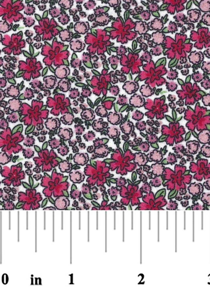 A close-up of a floral fabric pattern featuring pink and magenta flowers with green leaves on a white background with a ruler at the bottom for scale.