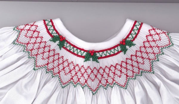 White dress with red and green smocked around the neck on a gray background