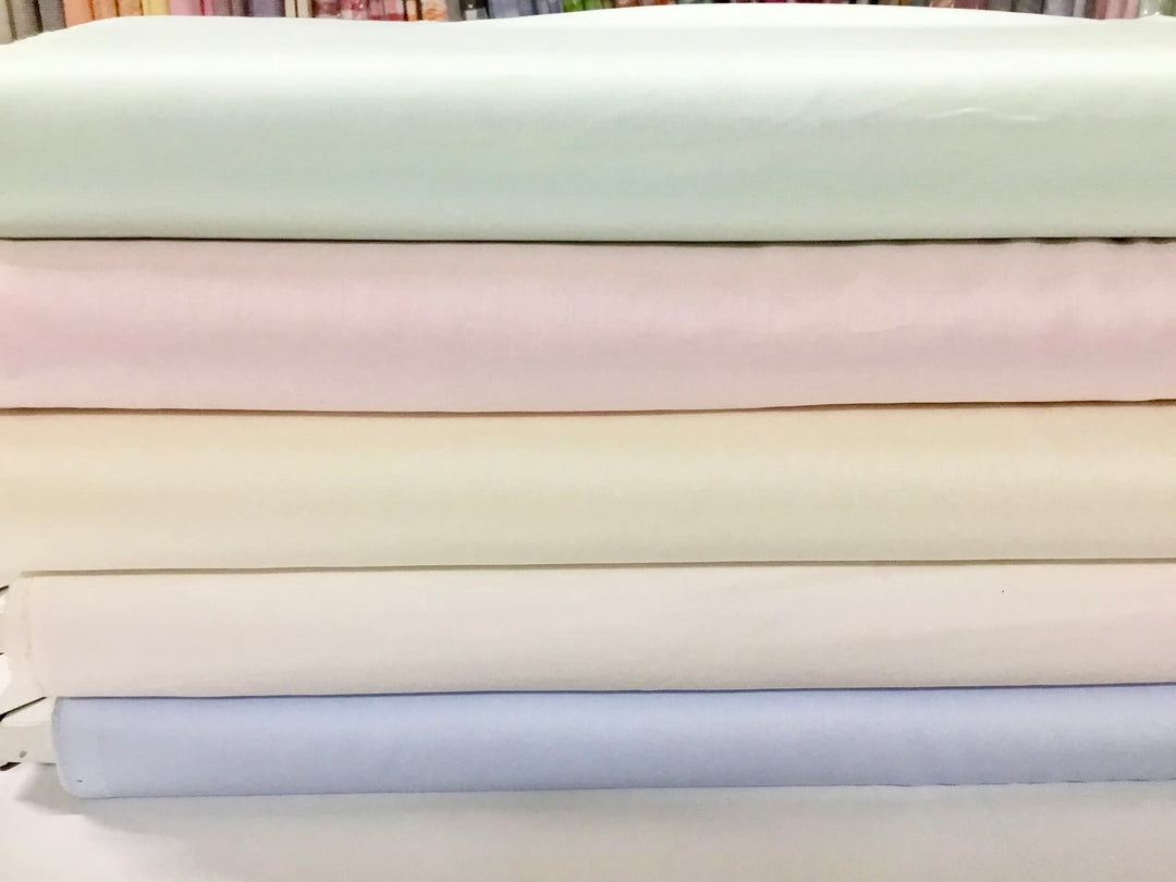 Stack of light-colored fabric swatches in pastel shades.
