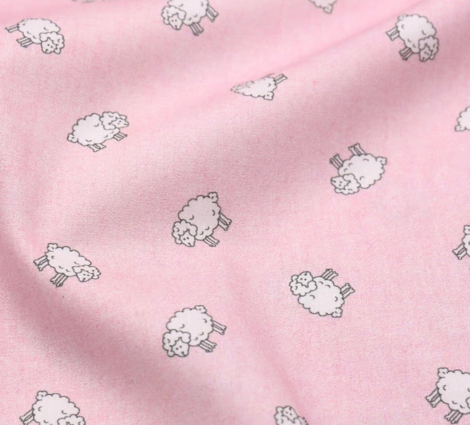 Pink fabric with a repeating pattern of small white cartoon sheep outlined in dark gray, shown in a close-up with soft folds.