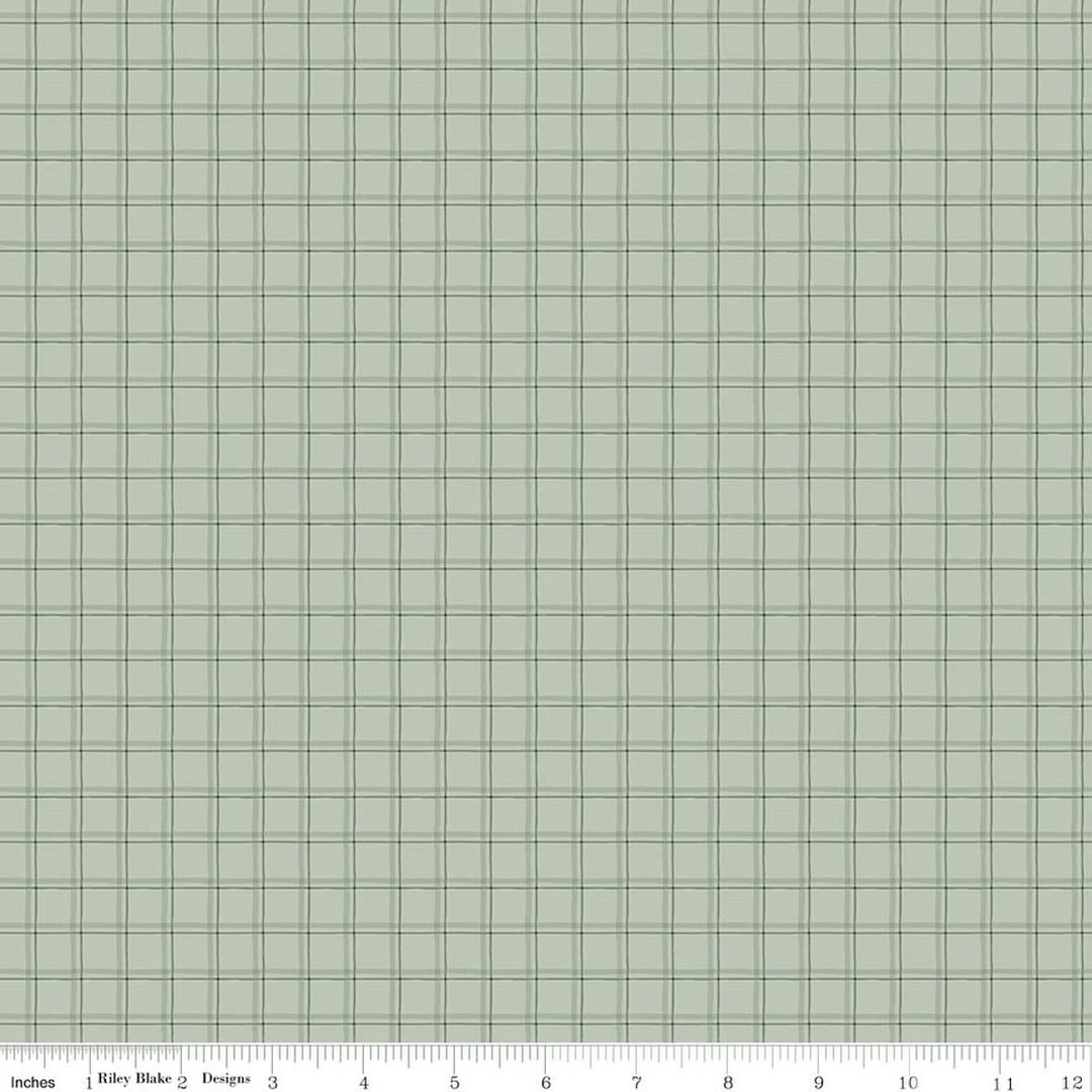 A close-up of a fabric or material swatch with a light sage green background and a fine dark green grid pattern. A ruler scale along the bottom edge shows inches and includes the text 'Riley Blake Designs', indicating the brand.