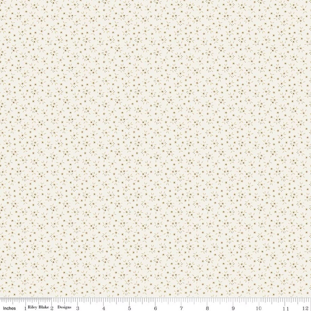 A close-up of a fabric pattern featuring tiny brown and muted gold floral motifs on a warm cream background, with a measuring ruler visible along the bottom edge.