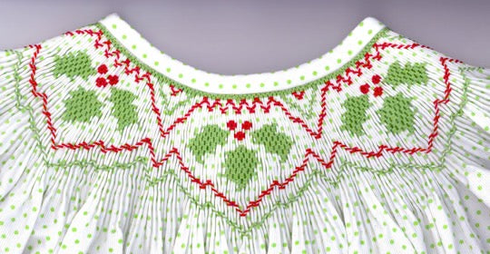 Close-up of a smocked neckline with green and red embroidery on a white fabric background.