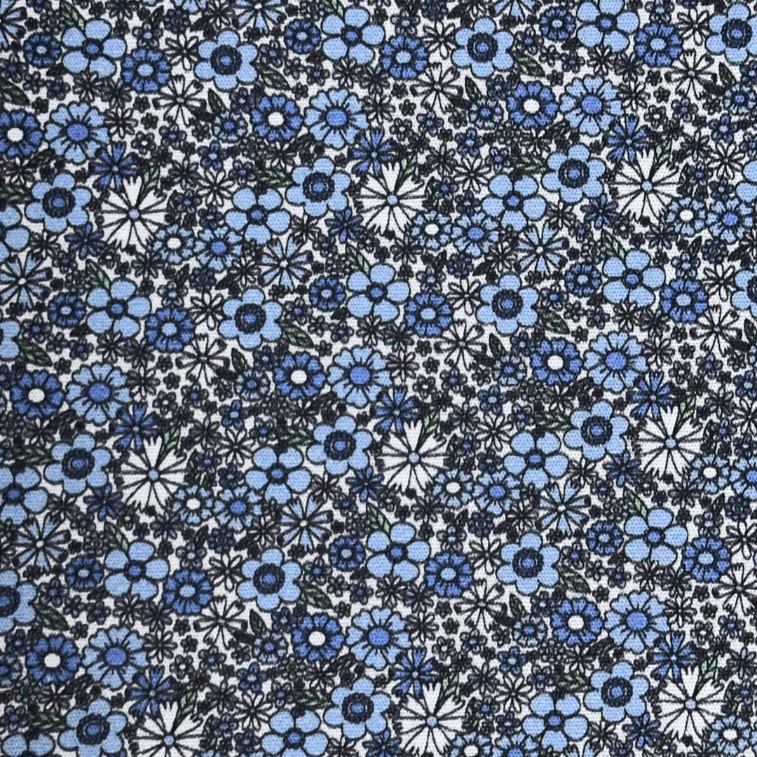 A close-up of a fabric pattern featuring small blue, navy, and white floral and starburst motifs on a white background.