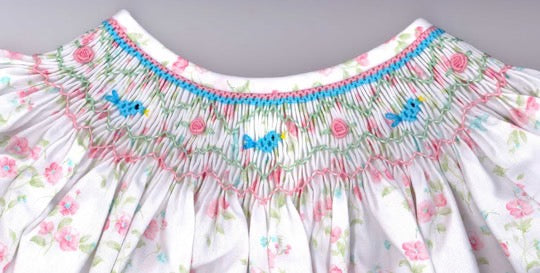 Floral dress with smocked neckline and blue butterfly details on a gray background