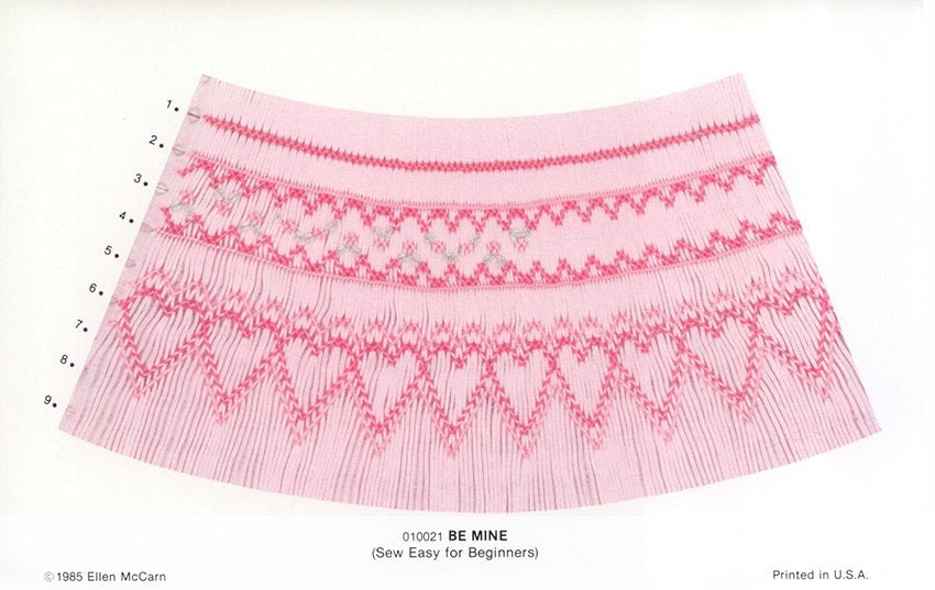 Smocking plate with a geometric design on pink pleated fabric smocked in pinks with hearts and flowers. 9 rows of smocking on a bishop. 