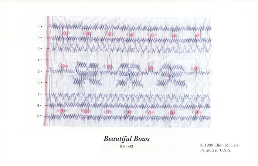 Smocking plate with blue bows and pink flowers in a geometric design on white pleated fabric. 9 rows of smocking on a yoke.  