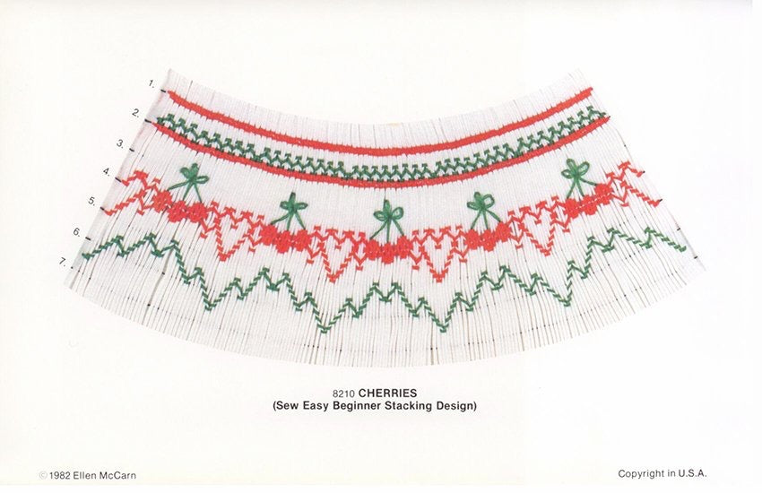 Smocking plate with a geometric design  smocked in green and red with red cherries. 7 rows of smocking on white pleated fabric