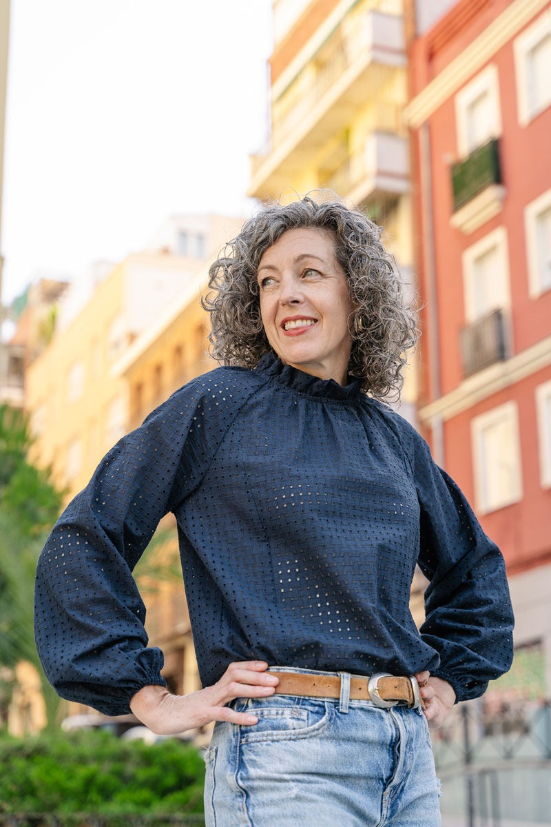 Woman wearing a dark blue blouse with puffed sleeves and light blue jeans standing in an urban setting.