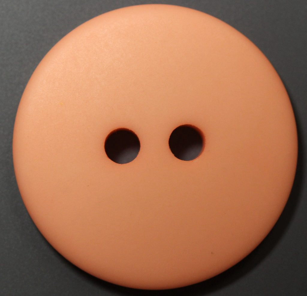 Close-up of a peach button with two holes on a dark background