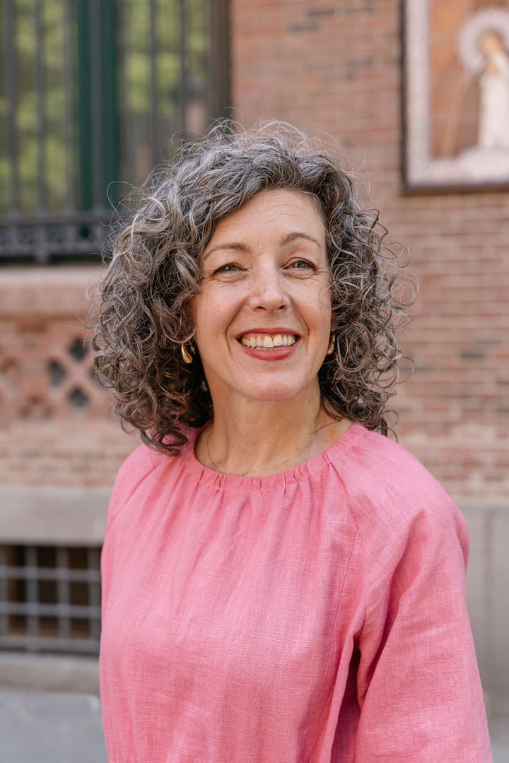 Woman with gray hair wearing a pink top in front of a brick wall.