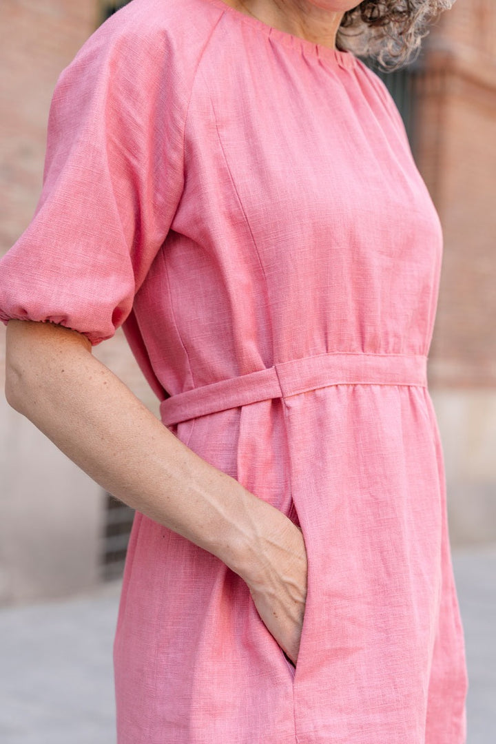 Person wearing a pink dress with a belt, standing against a blurred background