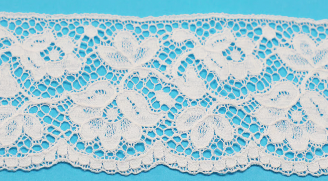 White floral lace trim with an intricate openwork pattern and scalloped edge, displayed horizontally against a bright blue background.
