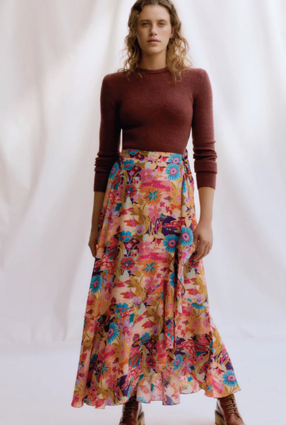 Woman wearing a brown top and colorful floral skirt on a white background