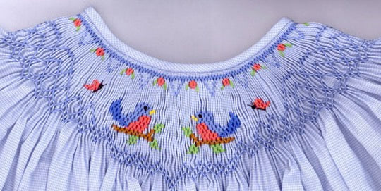 Close-up of a blue smocked dress with embroidered birds on a plain background