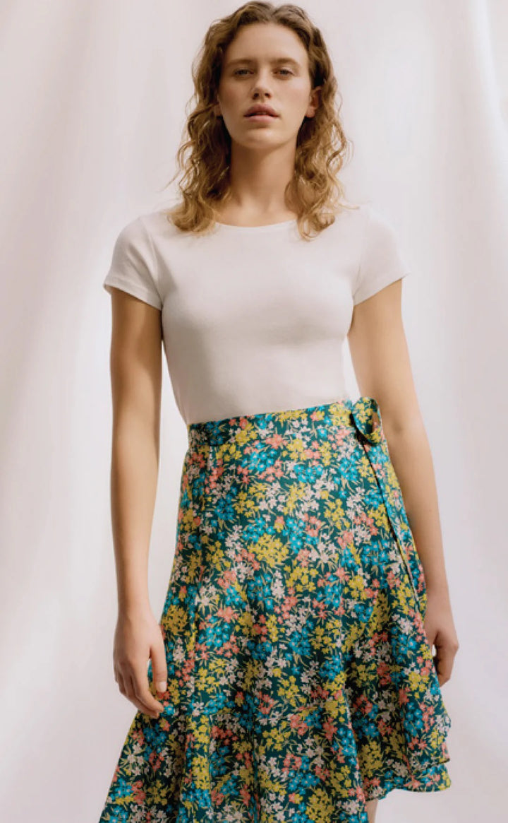 Woman wearing a white top and colorful floral skirt against a plain background