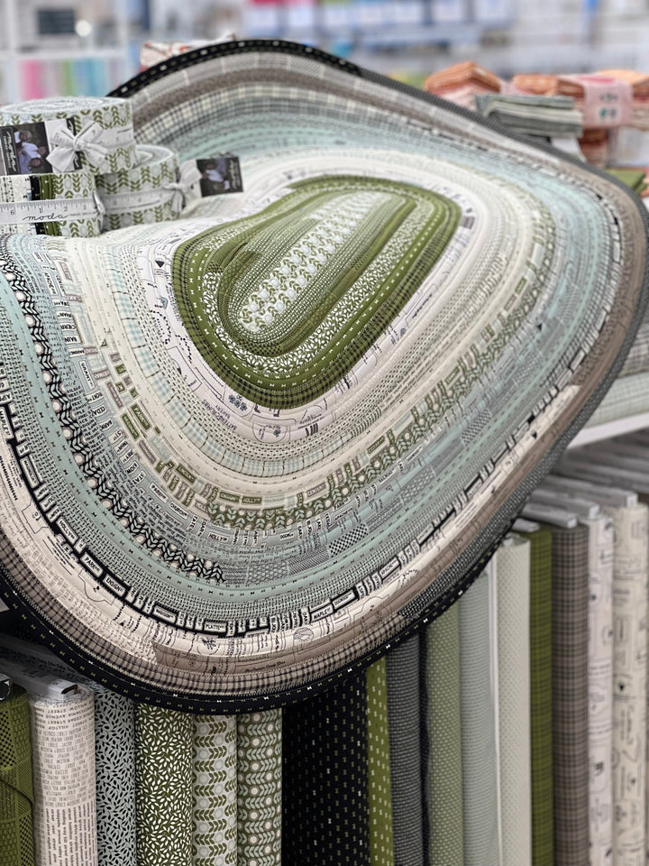 A jelly roll rug made from a combination of various fabrics, displayed in a store with the Sewing House logo visible.