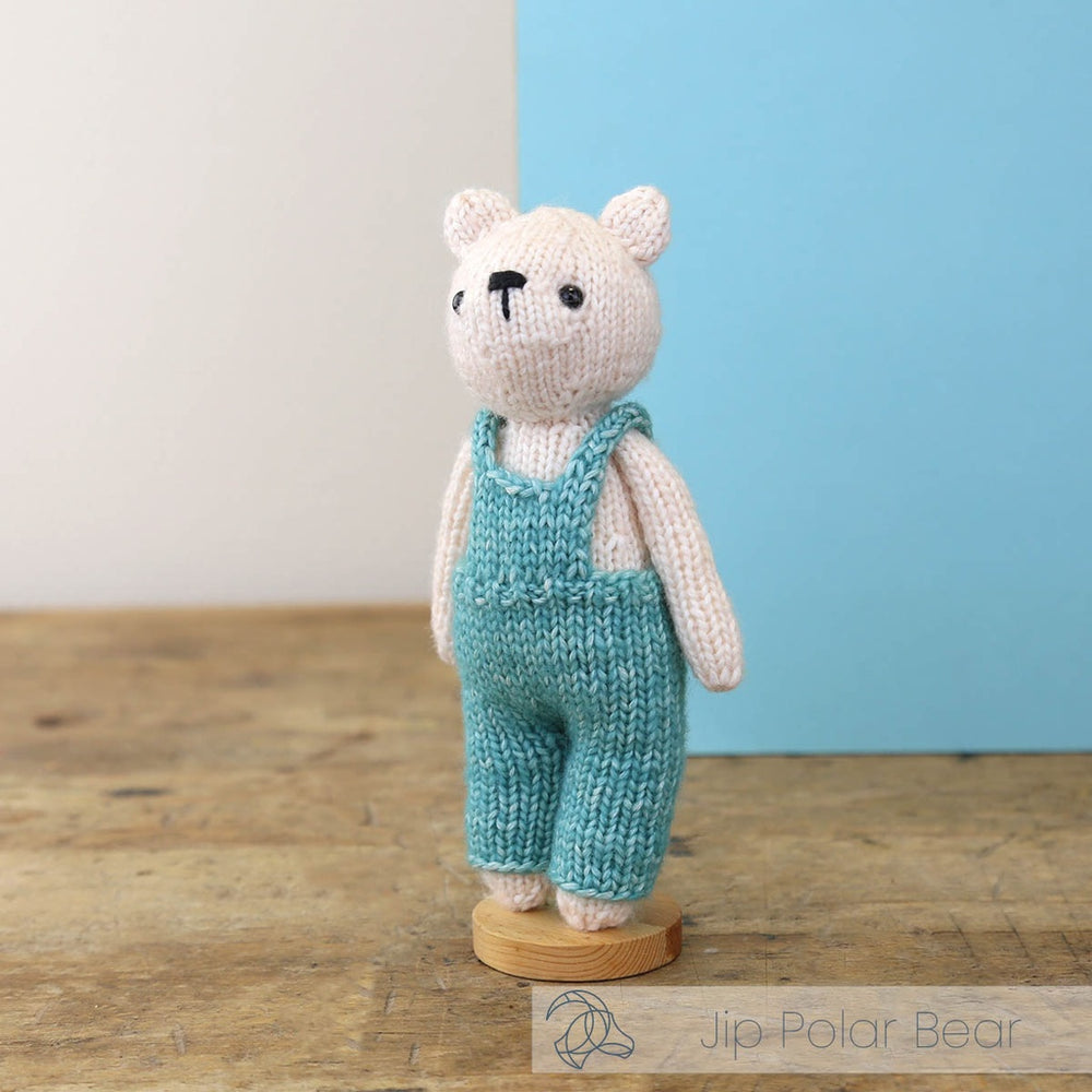 Knitted polar bear toy with blue overalls on a wooden surface with a light blue background