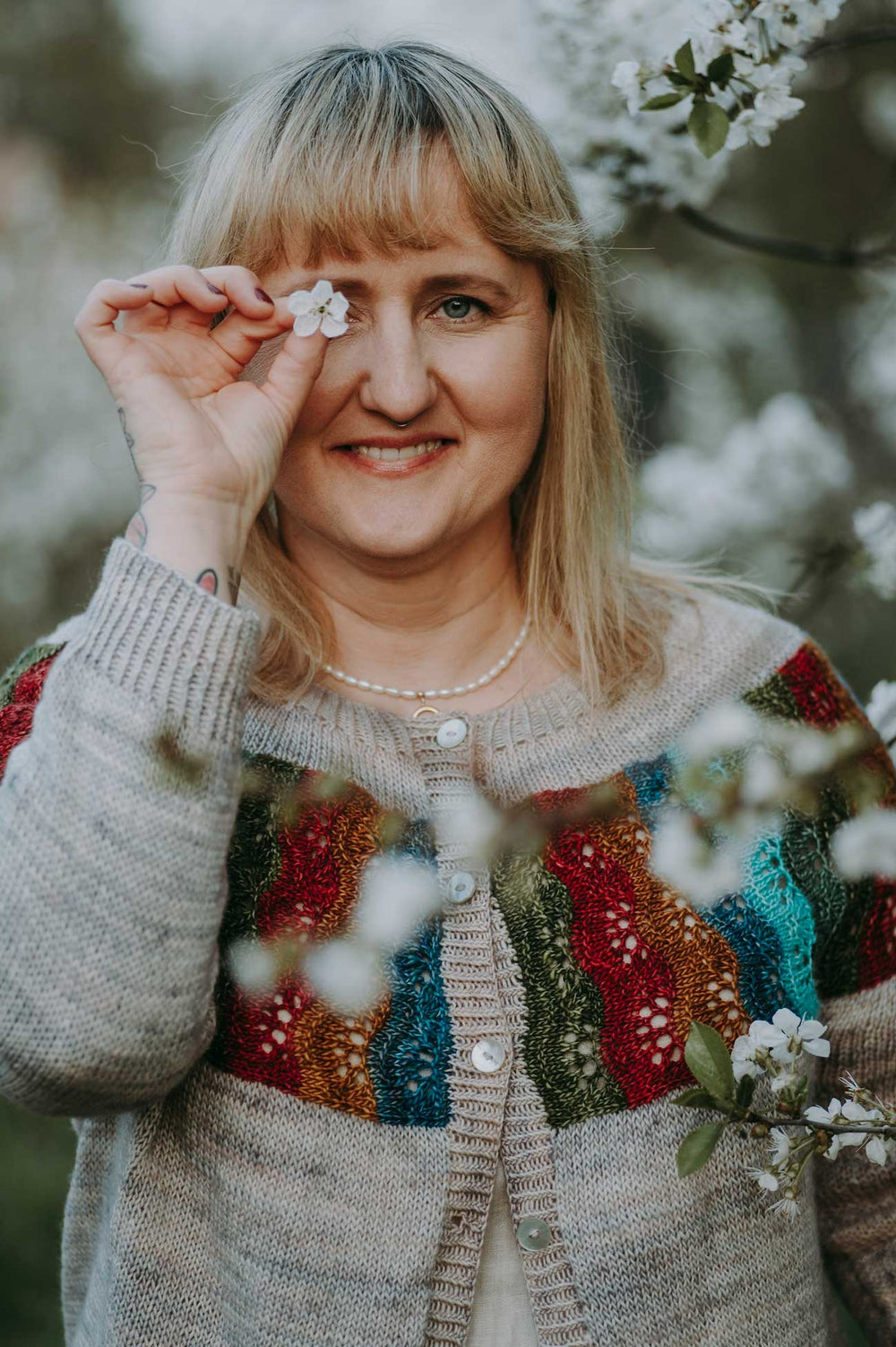Woman holding a flower to her eye with a colorful sweater and floral background