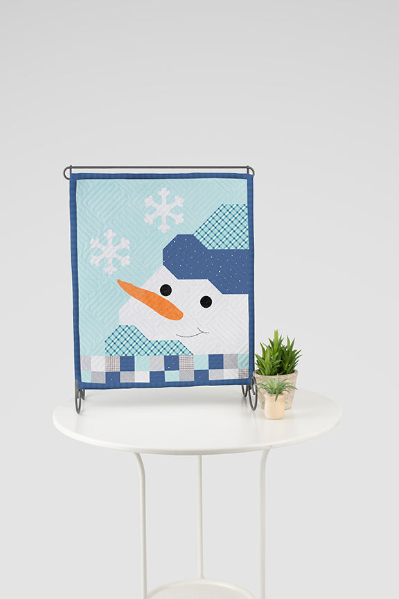 Decorative quilt with a snowman design on a white table against a light gray background