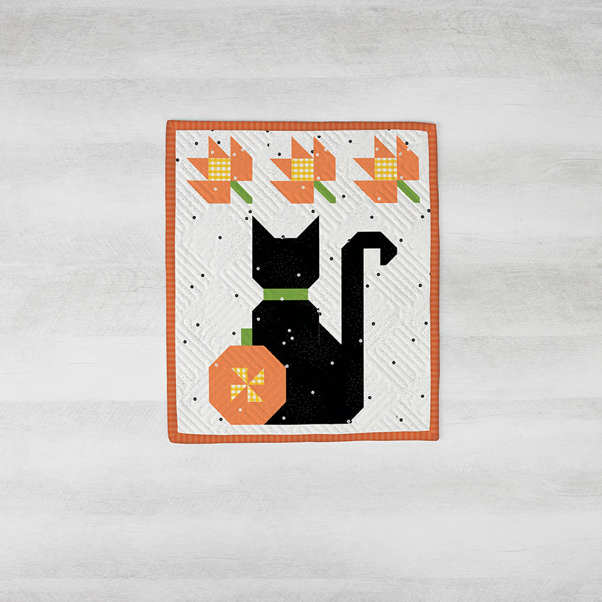 Quilt block with a black cat, orange pumpkin, and flowers on a white background