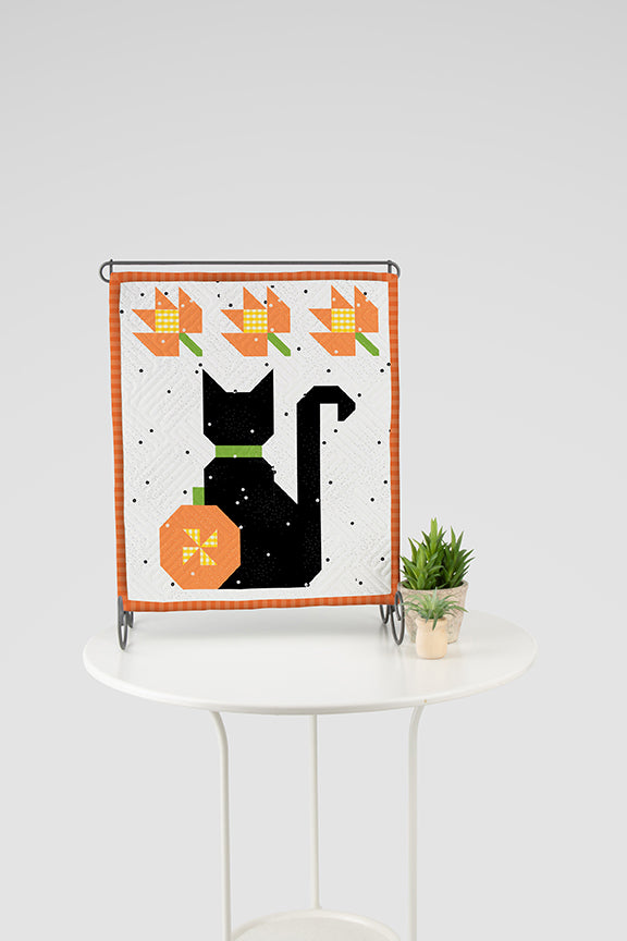 Decorative table top banner with a black cat and pumpkins on a white table against a light gray background
