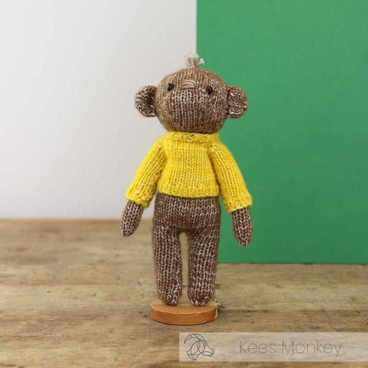 Knitted monkey toy wearing a yellow sweater on a wooden surface with a green background